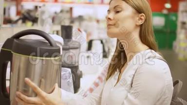 年轻女子在商店买厨房用具。 拿起热水瓶，选择水壶